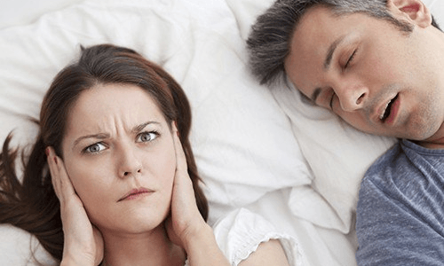 Woman with hands over her ears because sleep partner is snoring